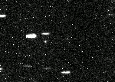Image avec une petite tache blanche qui se déplace au milieu des étoiles appraissant comme de petites lignes lumieuses.